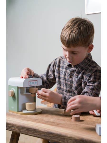 Person hælder vand i lille kaffemaskine på træbord med kopper og tilbehør ved siden af